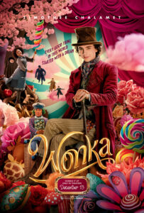 Willy Wonka stands triumphantly surrounded by edible flowers with the supporting cast integrated into the background
