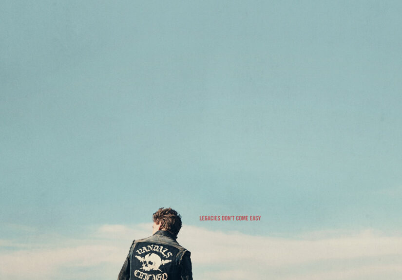 Austin Butler sits on a 60s Harley Davison motorcycle at the side of a road, looking out toward the flat horizon