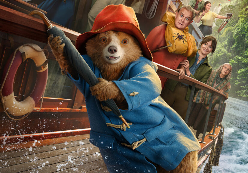 Paddington hangs off the side of the river boat by his umbrella as the rest of the Brown family, the boat's captain and the reverend mother are seen in the background